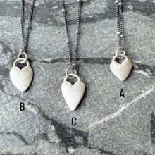 Three necklaces with heart-shaped pendants on a textured surface