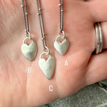 Three silver heart-shaped pendants on a hand with a blurred background