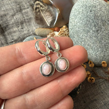 Silver earrings with pink stones held between fingers on a textured fabric background