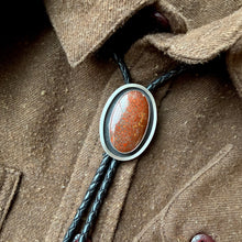 Close-up of a bolo tie with a brown stone pendant on a brown shirt