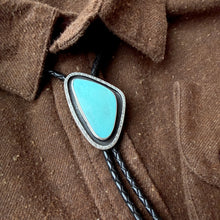 Turquoise stone bolo tie on a brown shirt