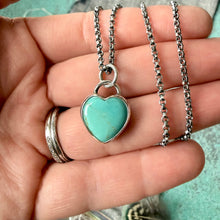Turquoise heart-shaped pendant on a silver chain held in a hand.