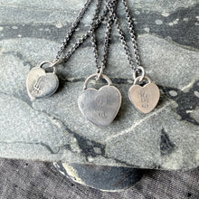 Three silver heart-shaped pendants on chains against a stone background
