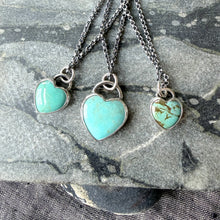 Three heart-shaped turquoise pendants on silver chains against a stone background