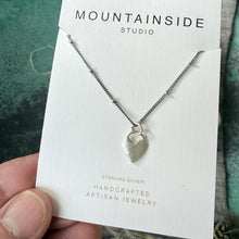 Silver necklace on a Mountainside Studio card held by a hand.