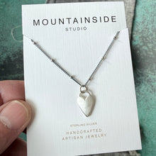 Silver necklace on a Mountainside Studio card held by a hand against a textured surface.